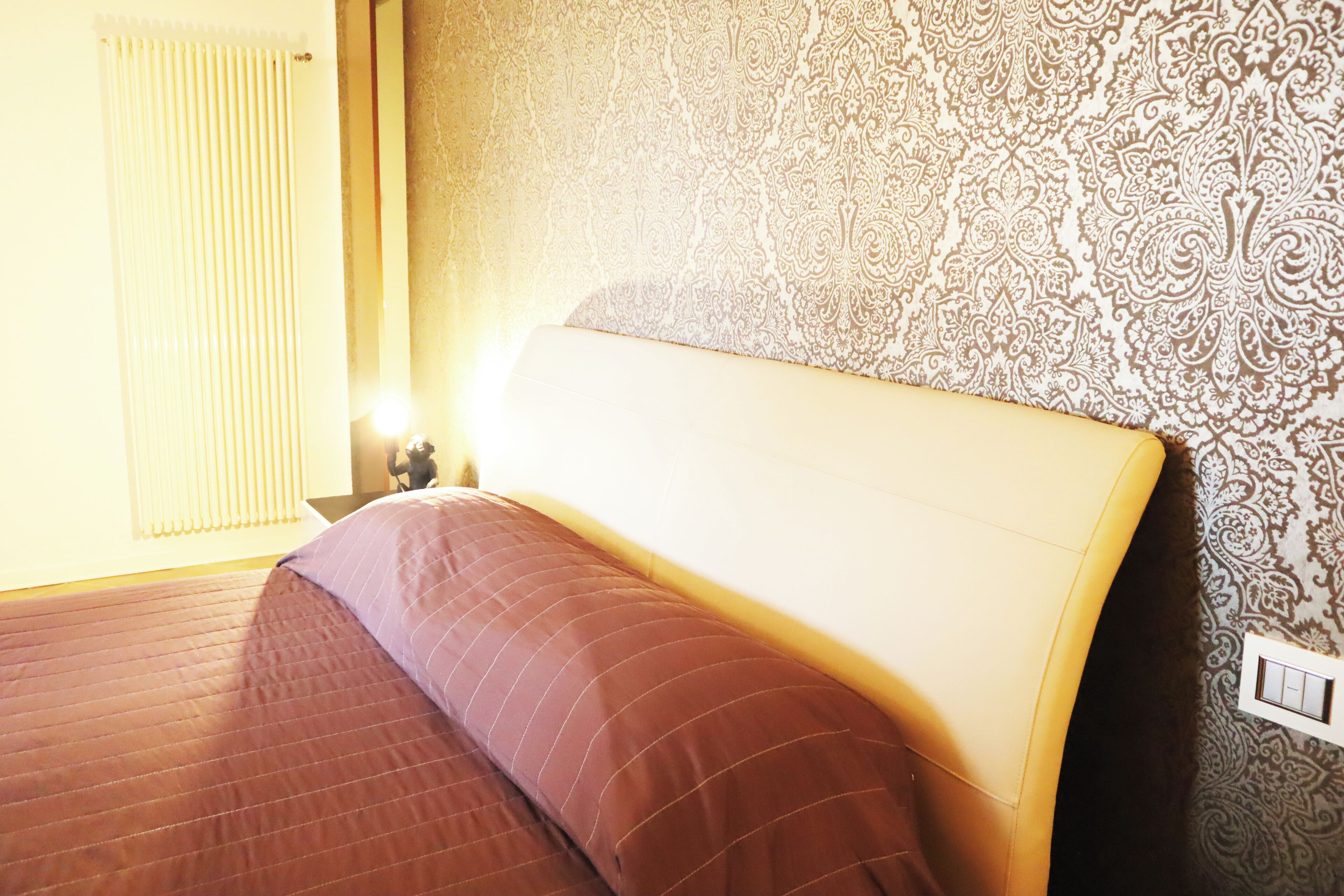 A hotel room with a bed, a nightstand, a lamp, and a patterned wall.
