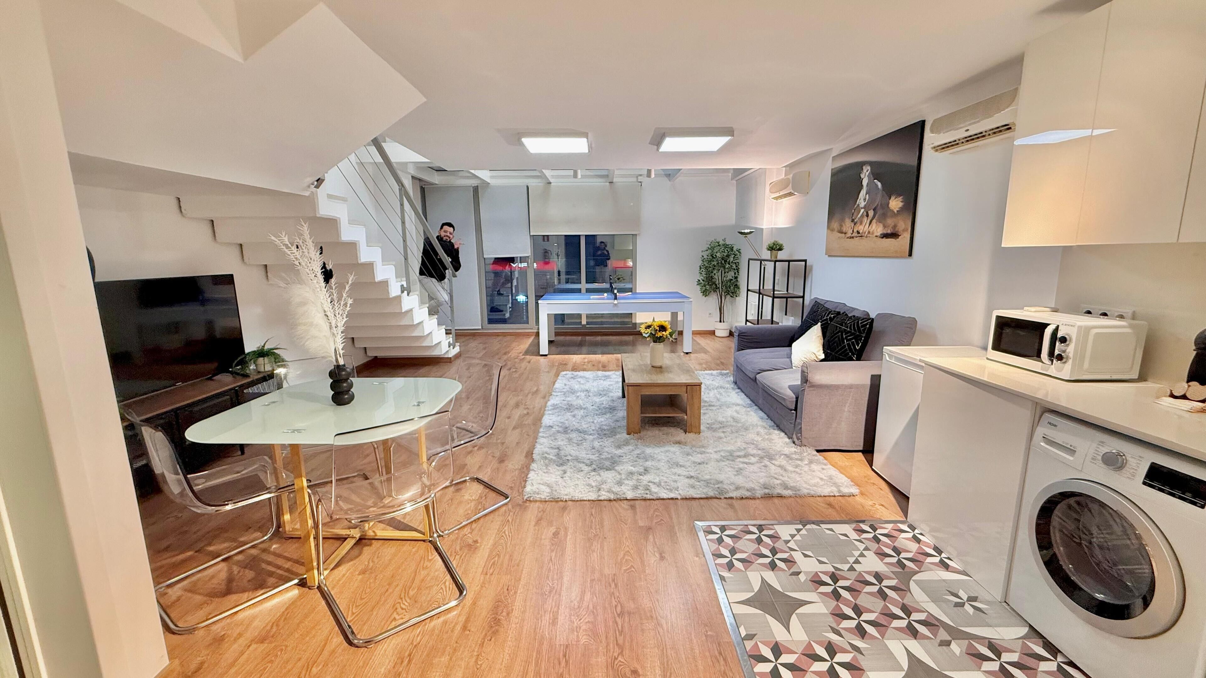 A modern apartment with a kitchen, dining area, living room, and a staircase leading to an upper floor.