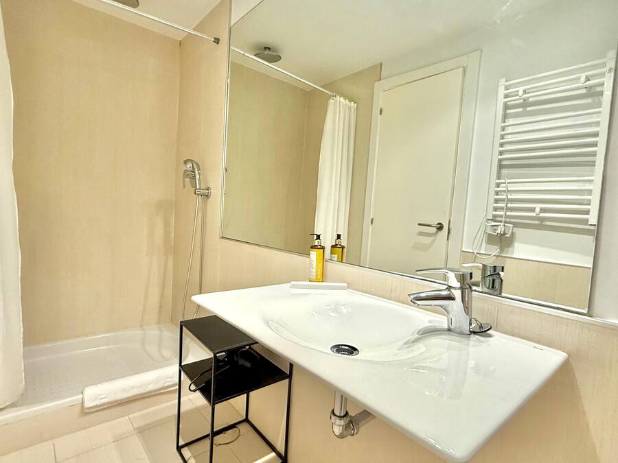 Un baño moderno con un lavamanos blanco, un espejo y una ducha.