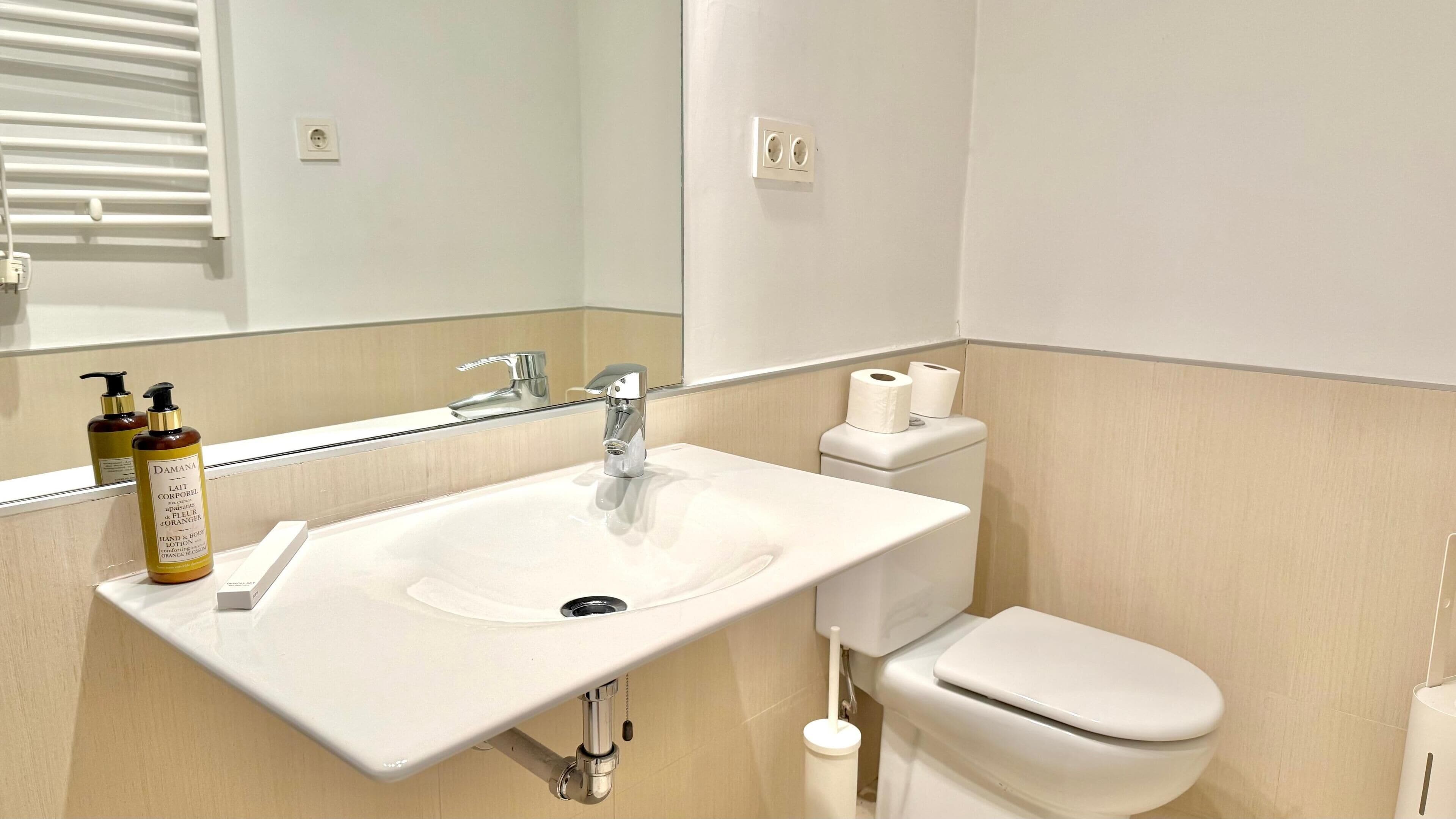 Un baño con un lavamanos blanco, un espejo, un inodoro y una botella de loción.