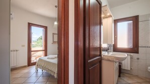 Een slaapkamer met een bed, een badkamer met een wastafel en uitzicht op het landschap.