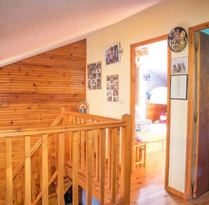 Eine Holztreppe führt zu einer zweiten Etage, mit einer Tür rechts und einer Wand mit Fotos und einer Uhr.