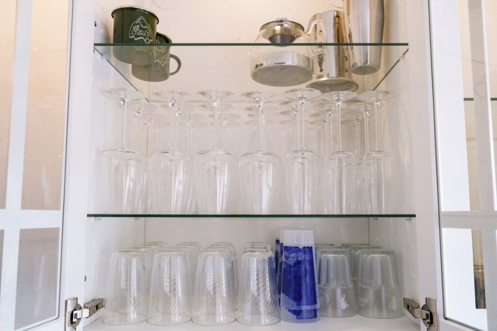 Une vitrine dont la façade est en verre, comportant plusieurs étagères où sont rangés des objets en verre transparent et un sac en plastique bleu.