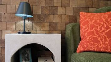 Rincón de una habitación con pared de madera, una mesita auxiliar blanca con lámpara, un sofá verde y un cojín estampado.