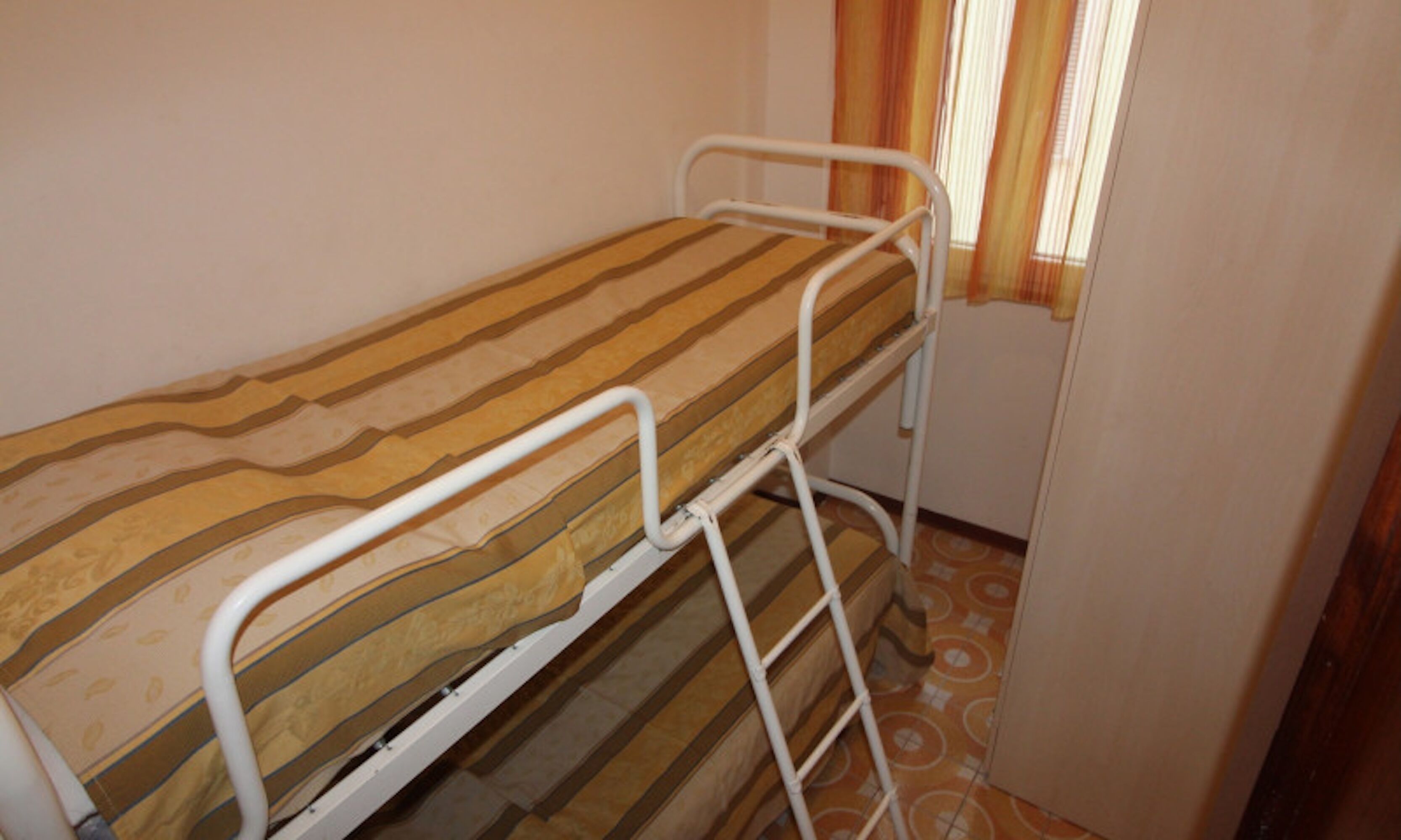 Una cama litera con un colchón a rayas en una habitación pequeña con ventana y cortinas.