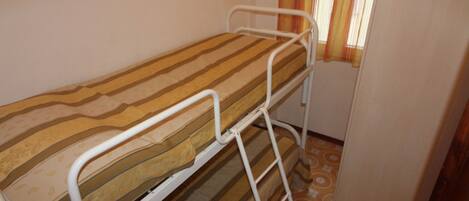 Una cama litera con un colchón a rayas en una habitación pequeña con ventana y cortinas.
