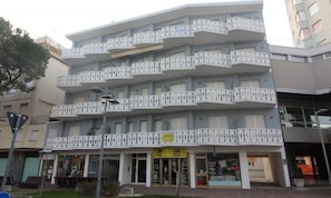 A multi-story building with balconies, a ground-level entrance, and a visible storefront. - Cozy Flat in the Heart of Lignano (Lignano Sabbiadoro)