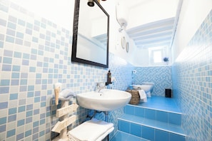 A bathroom with blue-tiled walls, a white sink, a mirror, and a toilet.
