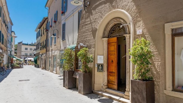 A narrow street with buildings on either side, a wooden door with a sign, and planters with small trees. - Residenza Ricasoli (Grosseto)