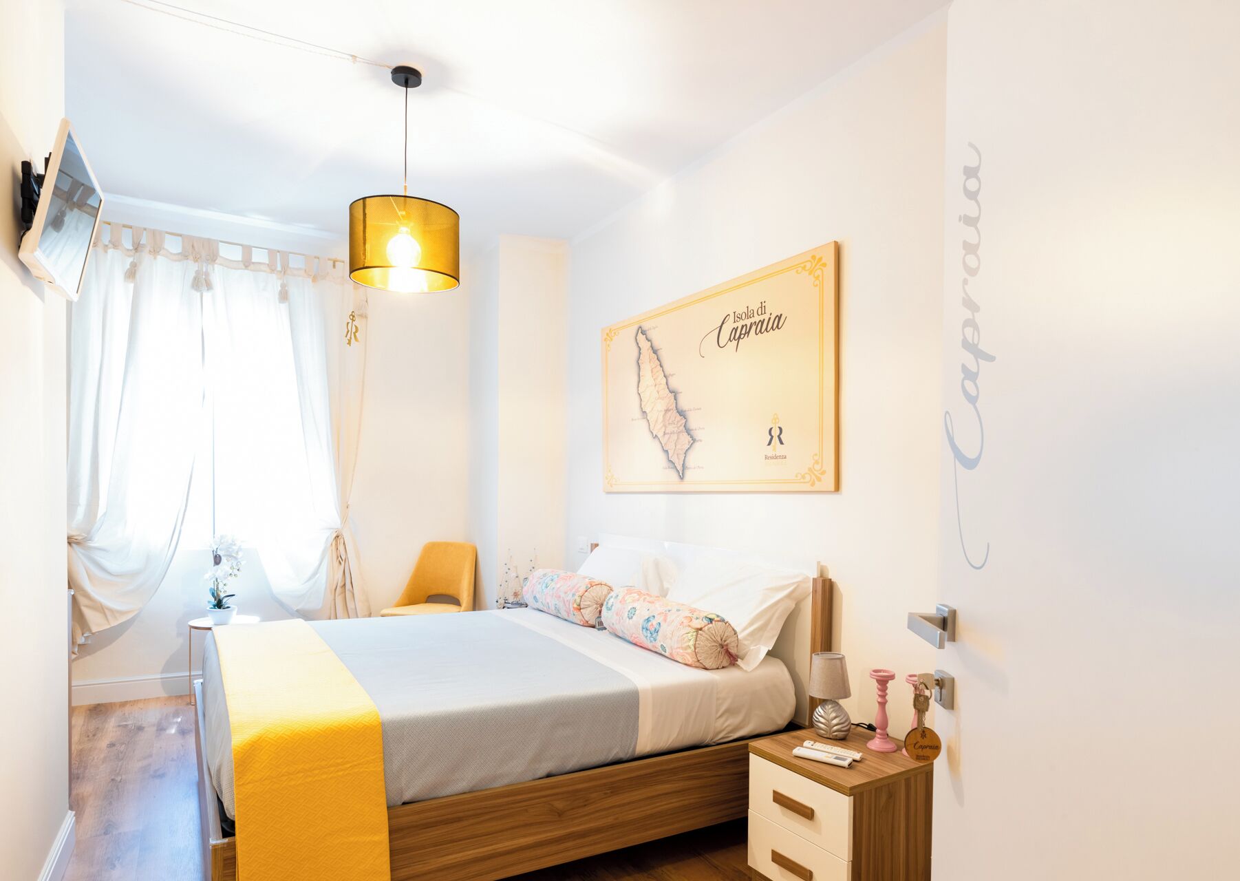 Un dormitorio con cama, mesitas de noche, una lámpara colgante, un mapa en la pared y una ventana con cortinas.