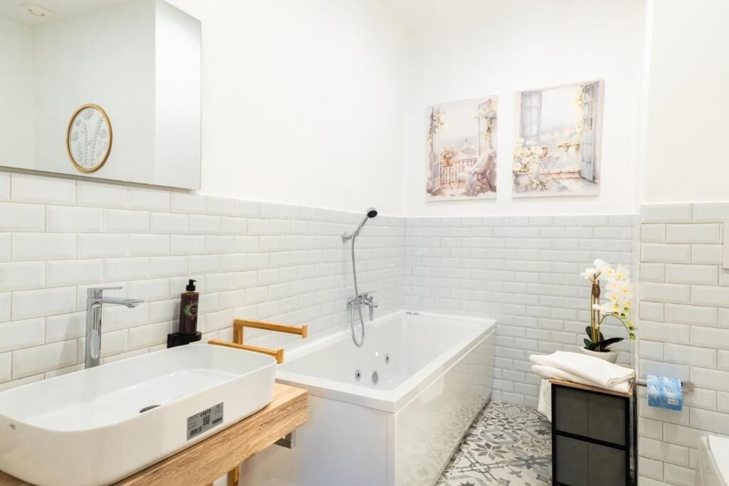 Une salle de bain moderne avec un lavabo blanc, une baignoire et une petite commode en bois.