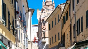 A narrow street with historic buildings, a prominent tower, and a red flag. - Residenza Ricasoli (Grosseto)