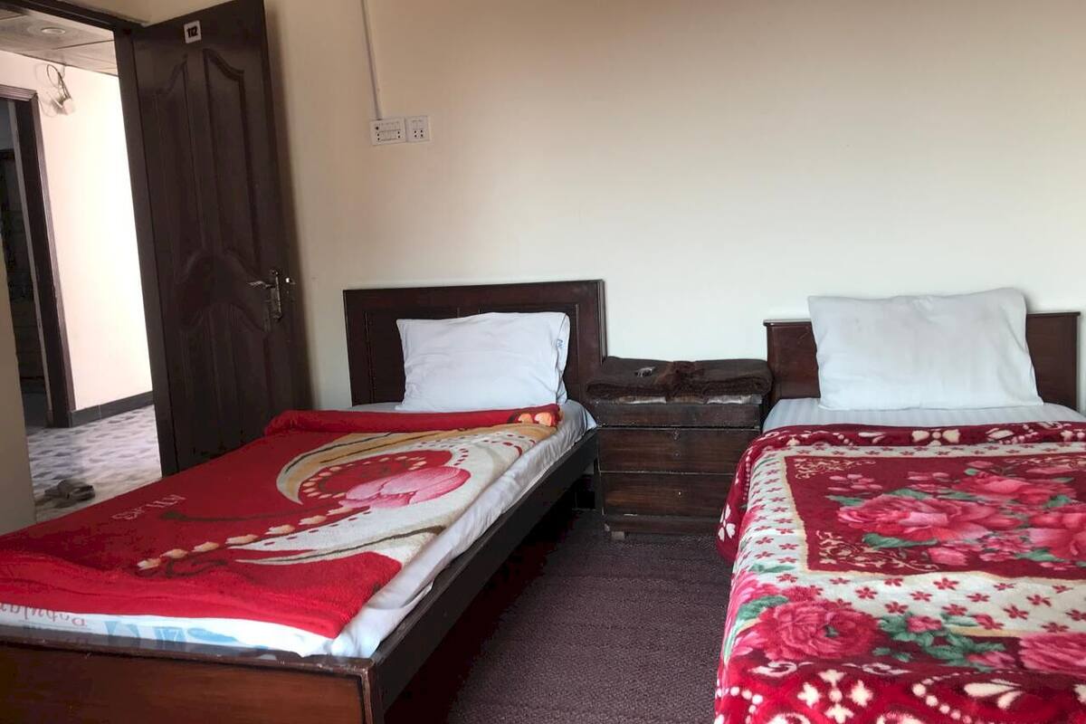 A room with two wooden beds, each with a white pillow and a red floral bedspread. There is a wooden dresser between the beds.