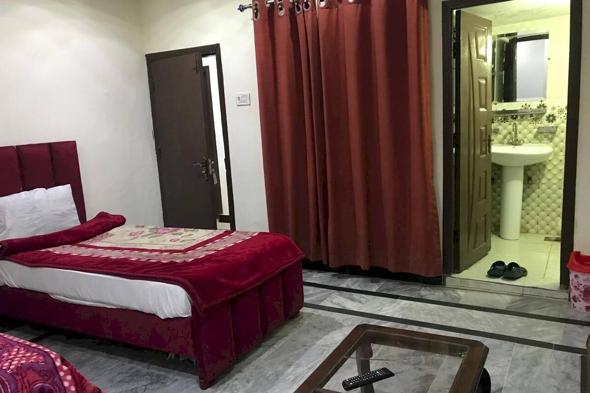 A hotel room with a bed, a small table, a bathroom visible through an open door, and a pair of slippers on the floor.