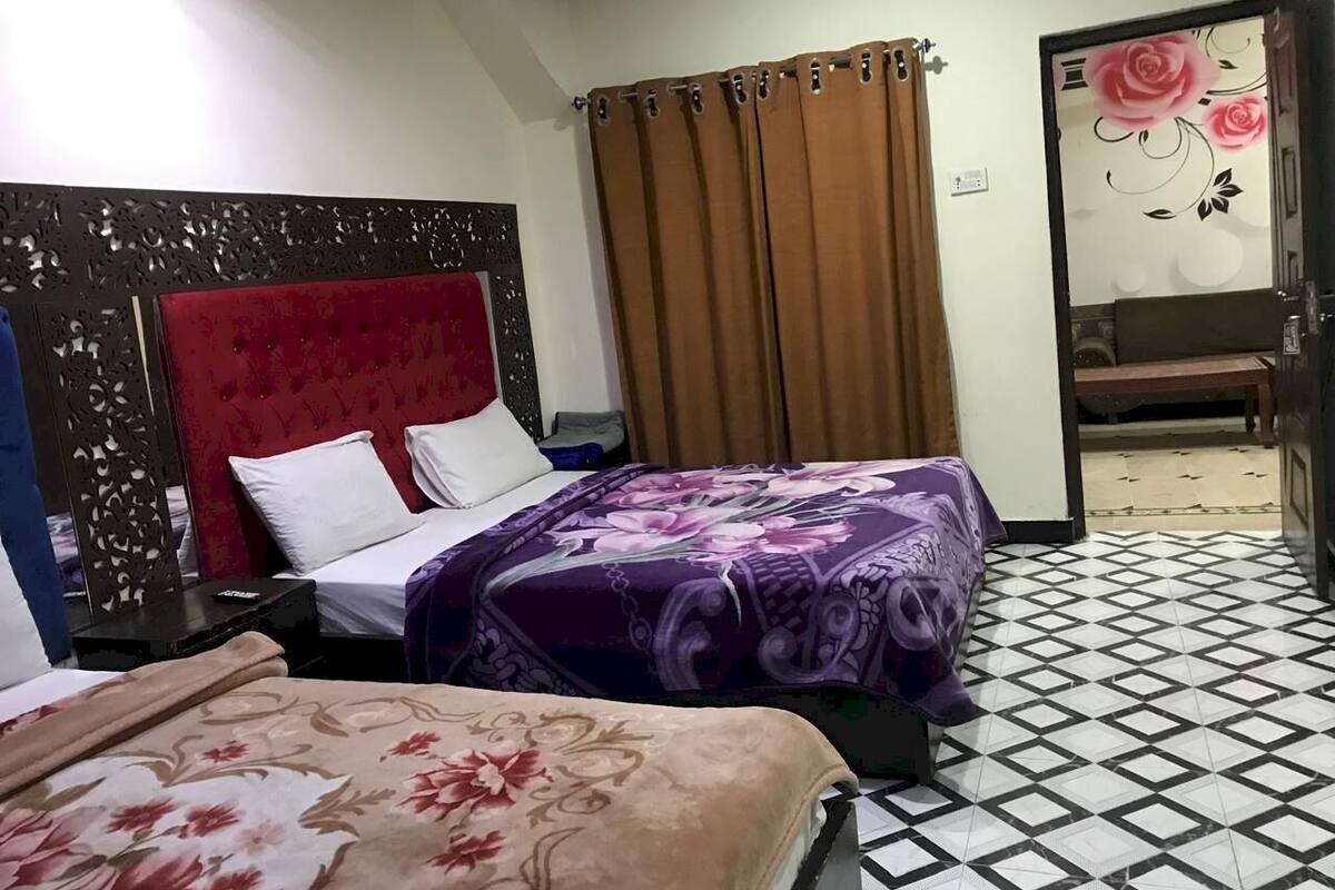 A hotel room with two beds, a red headboard, a patterned bedspread, a brown curtain, and a tiled floor.