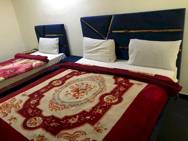A hotel room with two beds, each with a headboard, white bedding, and a red and beige patterned bedspread. - Dream IIN Hotel (Islamabad)