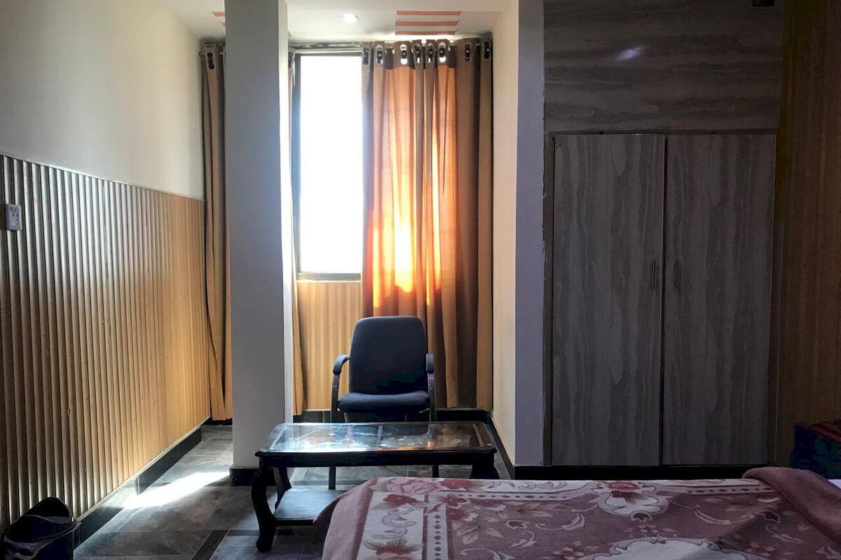 A hotel room with a bed, a chair, a table, a wardrobe, and a window with curtains.