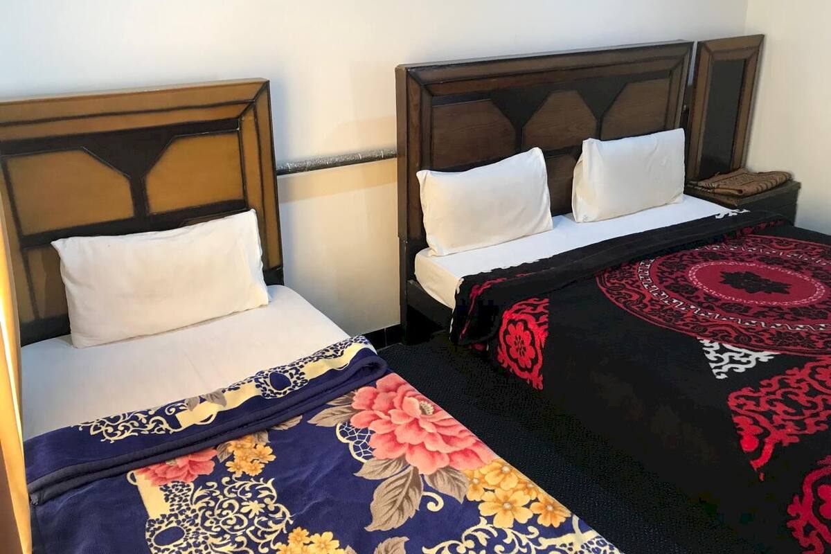 A hotel room with two single beds, each with a wooden headboard and white bedding. There is a decorative red and black rug on the floor.