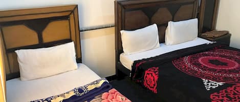 A hotel room with two single beds, each with a wooden headboard and white bedding. There is a decorative red and black rug on the floor.