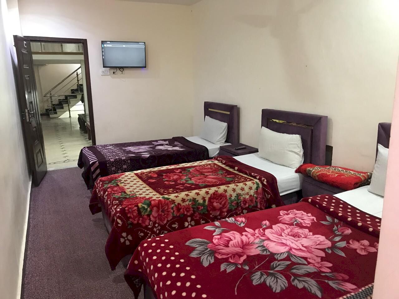 A hotel room with three beds, each with a different floral bedspread. There is a television mounted on the wall above the beds.