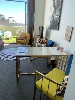 A modern hotel room with a dining table, yellow and blue chairs, a small TV, and a view of the cityscape. - Rendezvous Heritage studio with private balcony (Auckland)