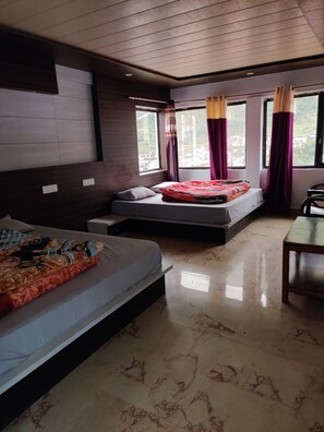A hotel room with a bed, a sofa bed, a small table, and a window with curtains. - Hotel Nanda Devi (Badrinath)