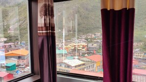 Une chambre avec un lit, une fenêtre avec des rideaux et une vue sur une ville avec ses bâtiments et ses montagnes.