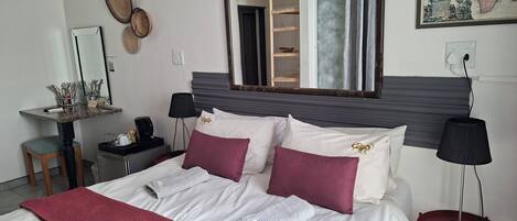 A neatly made bed with white and maroon bedding, a large mirror above it, a small desk with a lamp, and a map on the wall.