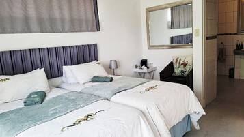 A hotel room with two beds, a bedside table with a lamp, a mirror, and a view into the bathroom.