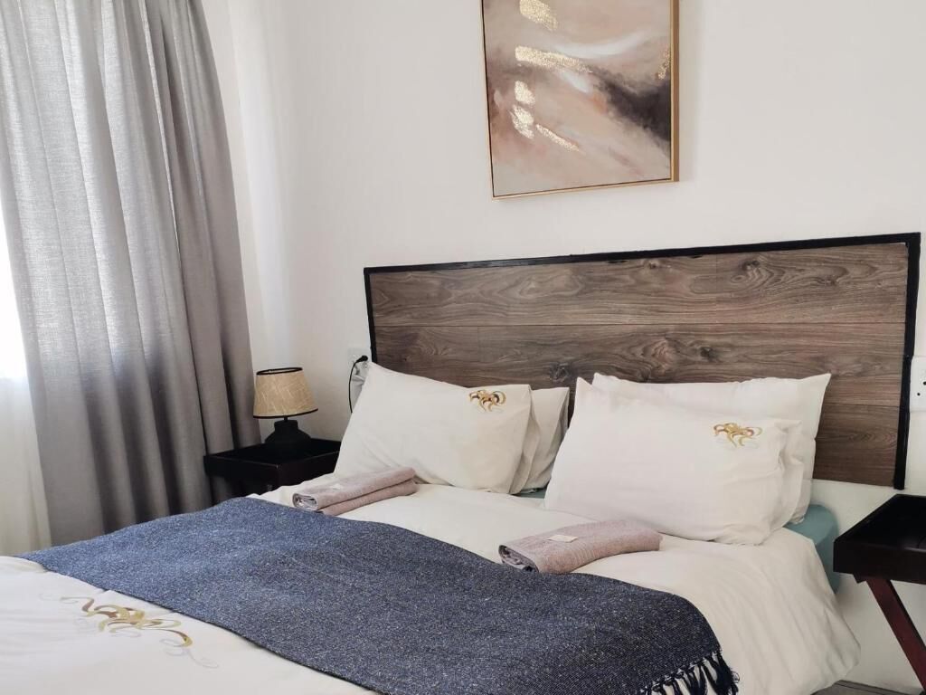 A neatly made bed with a blue blanket, a wooden headboard, and a wall-mounted abstract painting.