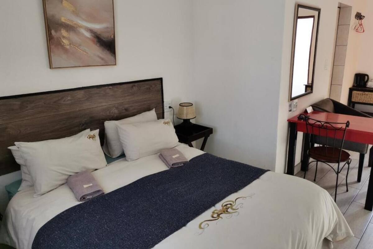 A neatly made bed with a dark blue blanket, a wooden headboard, and a wall-mounted abstract painting.