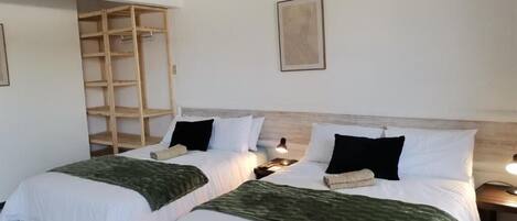 A room with two beds, each with white bedding and green throw blankets, wooden headboards, and bedside tables with lamps.