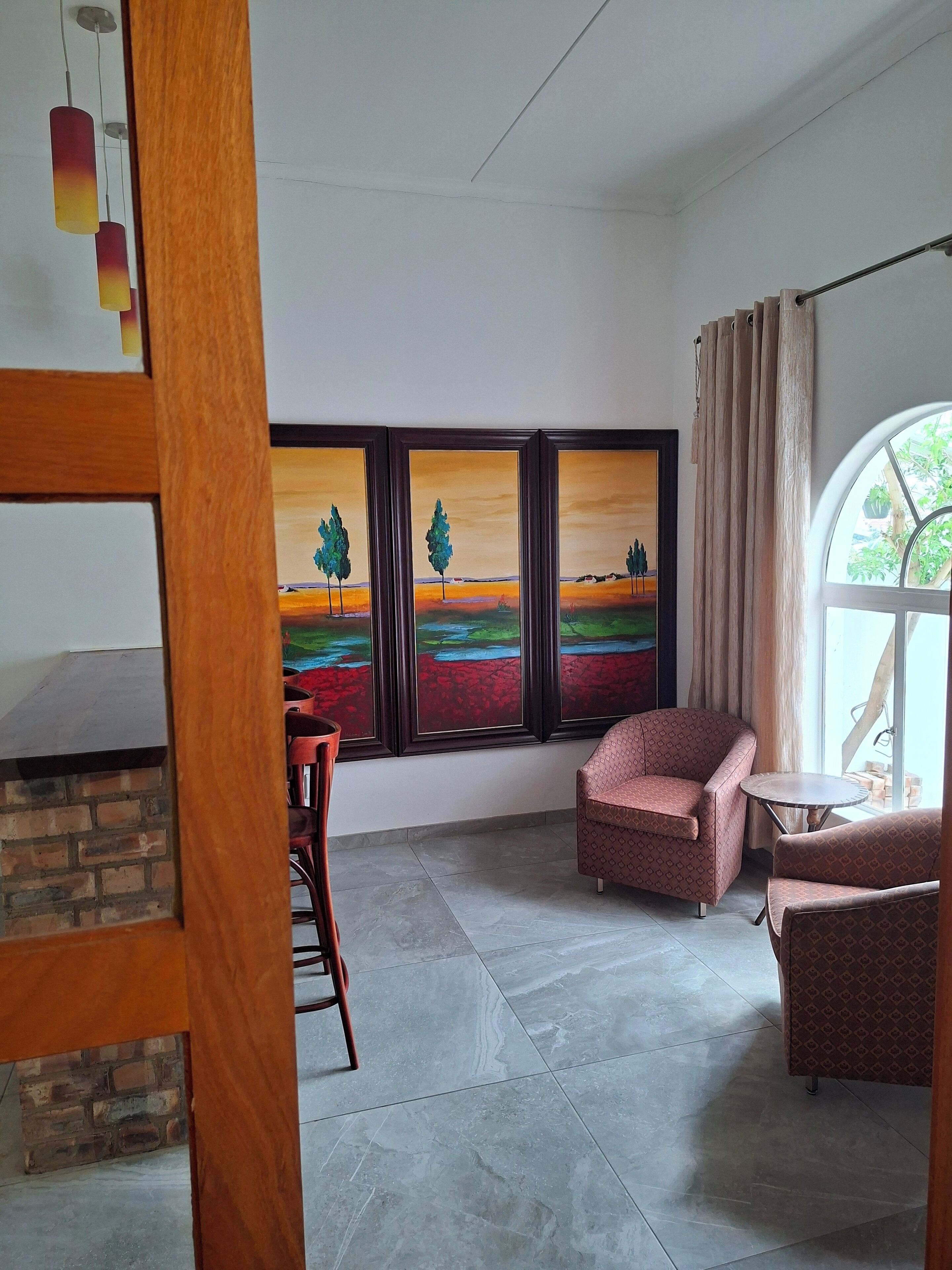 Een kamer met een open haard van baksteen, een groot raam met een schilderij, en twee gestreepten fauteuils.
