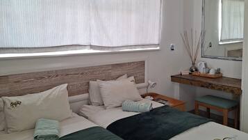 A neatly arranged bedroom with a large bed, a bedside table, a mirror, and a window with curtains.