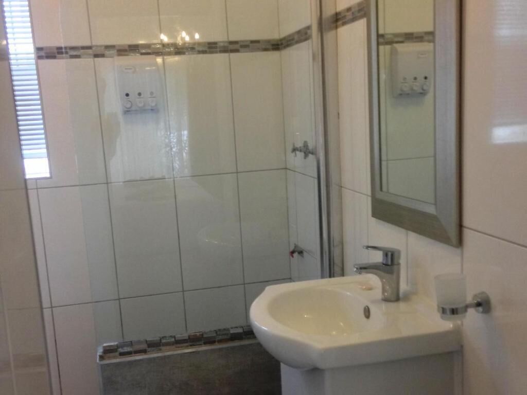 A bathroom with white tiles, a sink, a mirror, and a shower area.