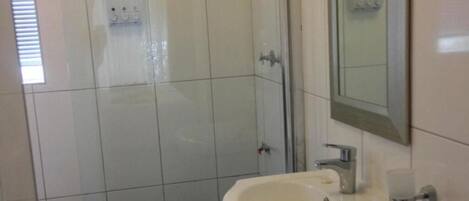 A bathroom with white tiles, a sink, a mirror, and a shower area.