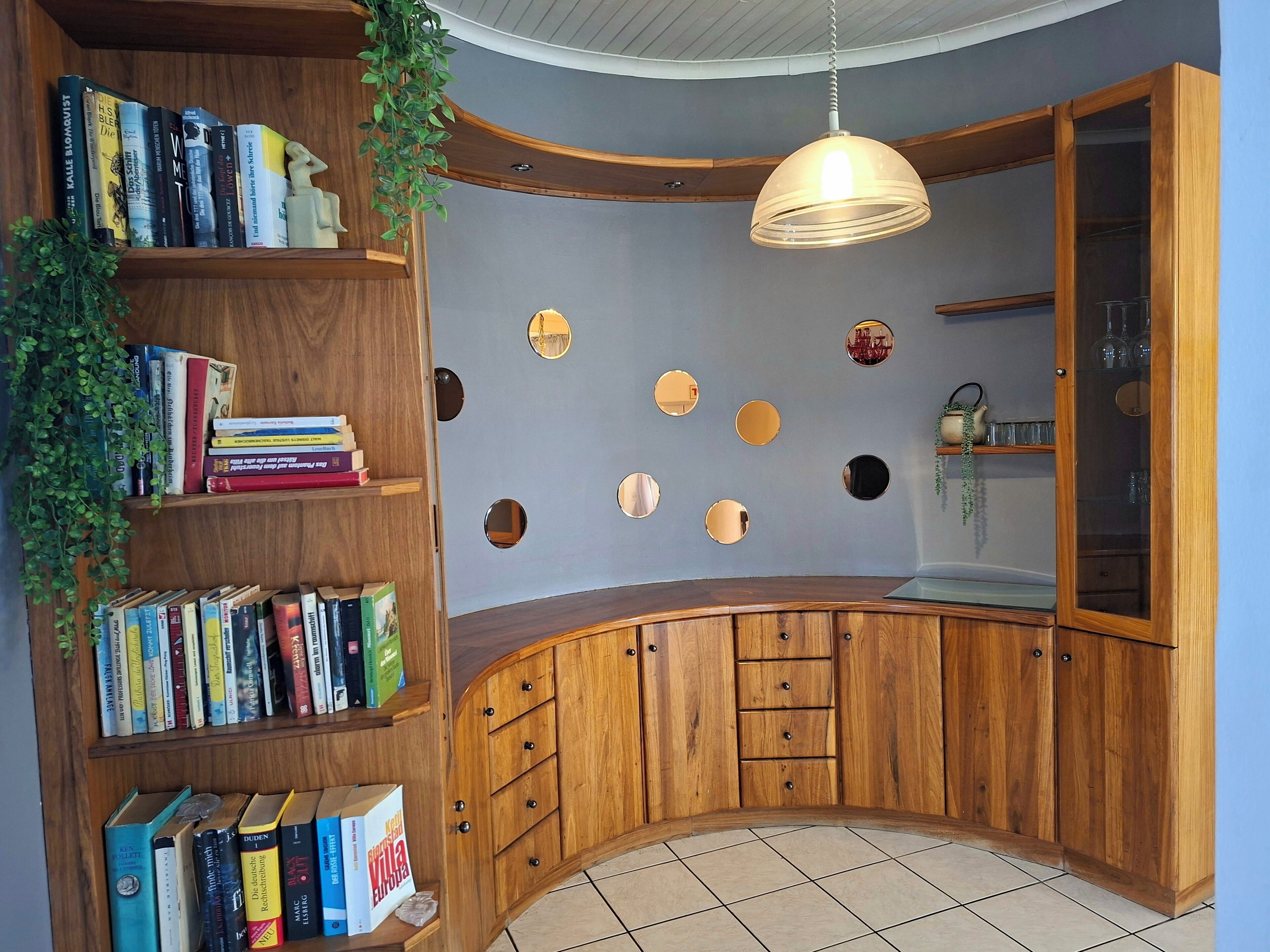 A room with wooden bookshelves filled with books, a curved wooden cabinet with drawers, and a hanging light fixture.