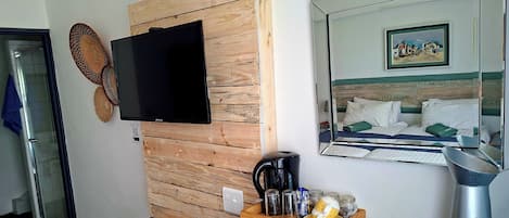 Ein Hotelzimmer mit einer Holzvertäfelung, einem Flachbildfernseher, einem Bett mit grünem Kopfteil, einem Nachttisch mit Kaffeemaschine, Gläsern und Vorratsgläsern.