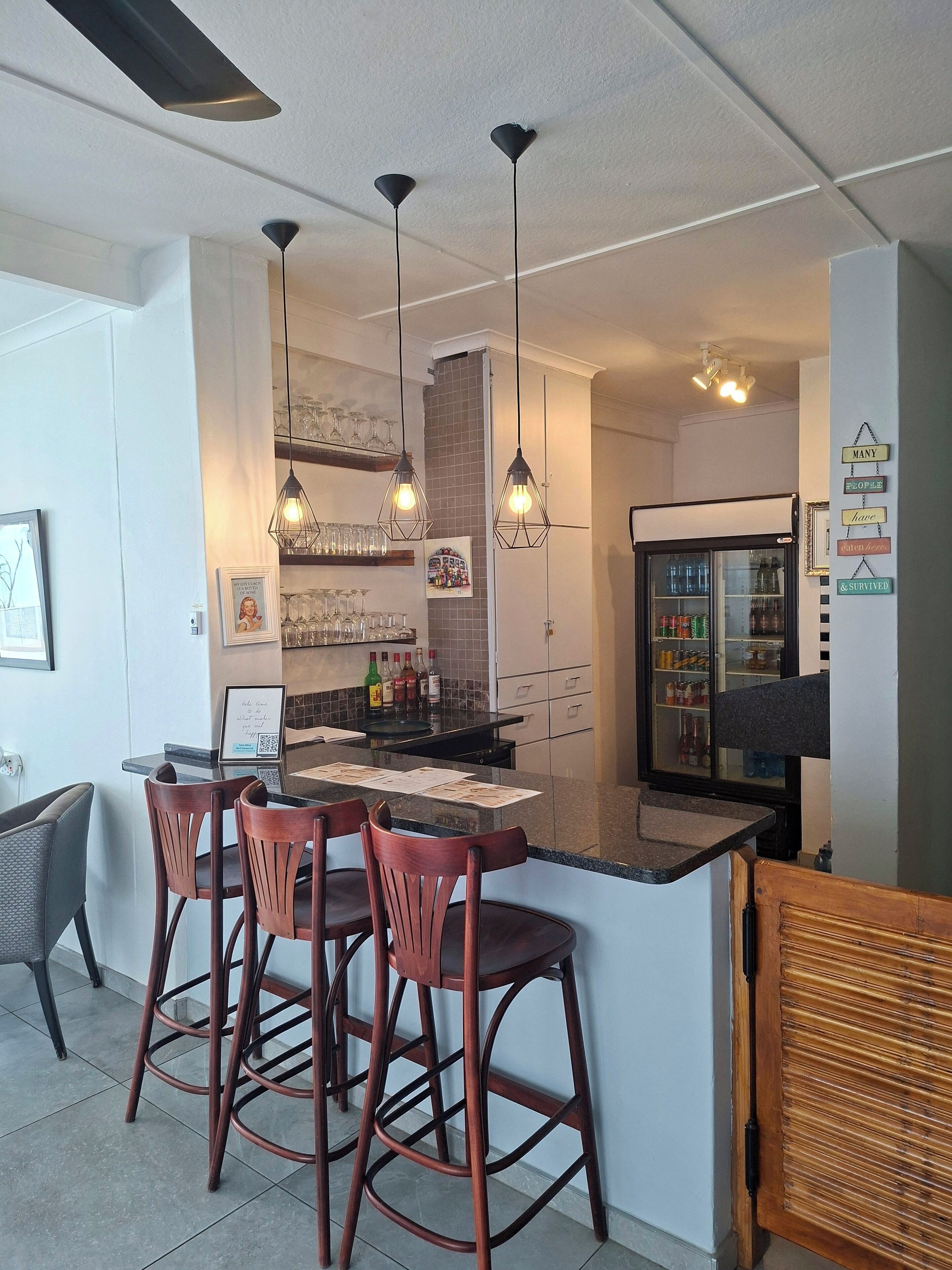 Una cocina moderna con una isla central, taburetes de bar, lámparas colgantes y un refrigerador.