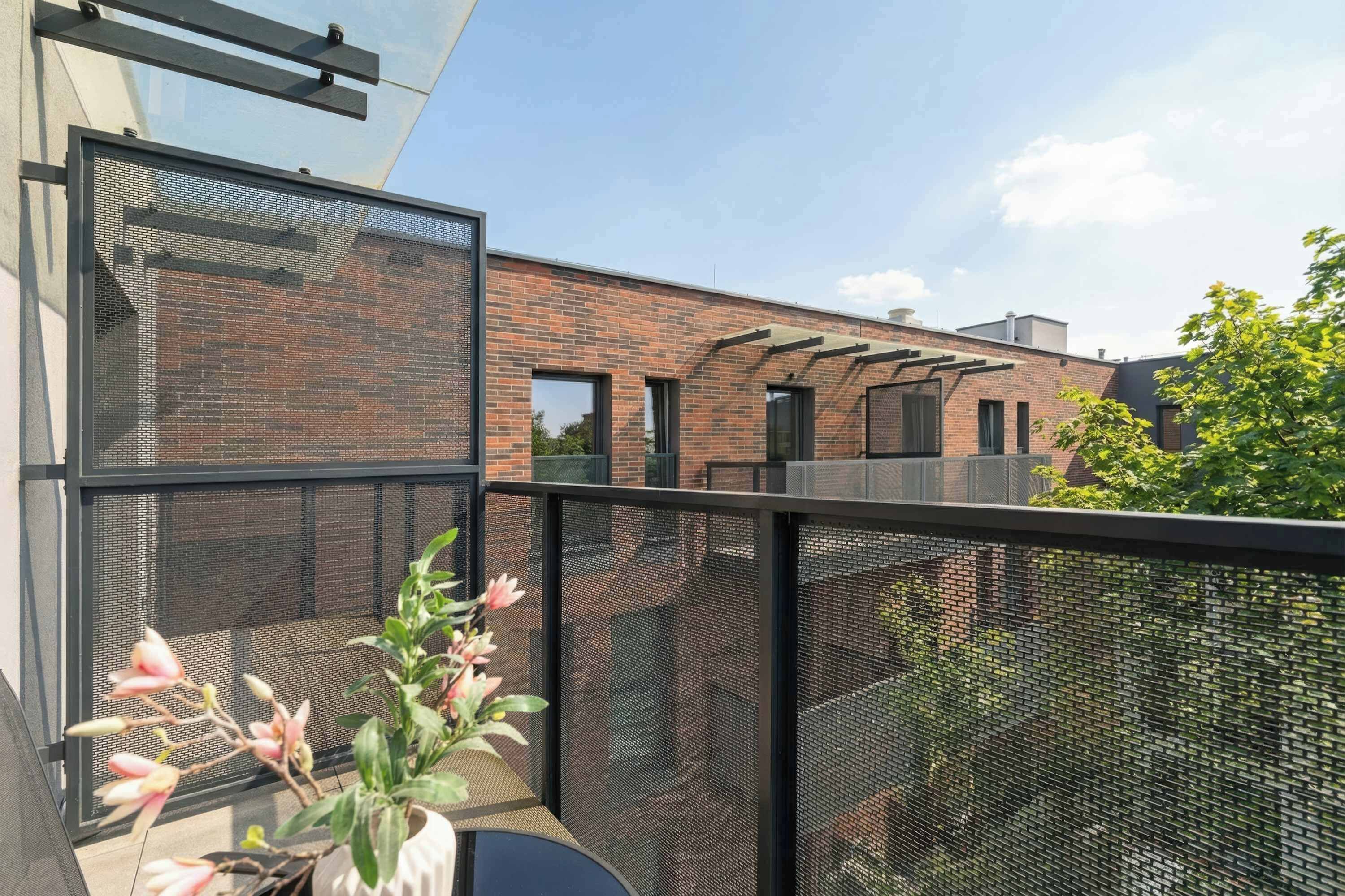 A balcony with a mesh screen, a potted plant, and a view of a brick building with windows.