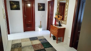 A hallway with wooden doors, a white tiled floor, a patterned rug, a wooden console table with a vase of flowers, and a decorative mirror. - Xaquina Apartment (Melide)