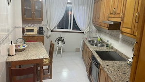 A kitchen with wooden cabinets, a granite countertop, a microwave, a sink, and a window with curtains. - Xaquina Apartment (Melide)