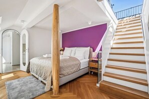 Ein Schlafzimmer mit Bett, Holzboden, einer lilafarbenen Akzentwand und einer Treppe.
