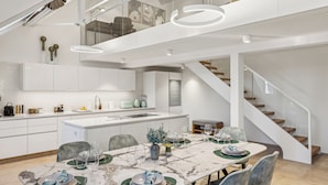 A modern kitchen with a marble countertop, a dining area with a table set for four, and a staircase leading to an upper level. - Old Town Penthouse | 360° Views | Rooftop Terrace (Zürich)