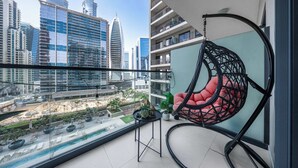 Ein Balkon mit Hängesessel, einem kleinen Tisch und Blick auf eine Skyline mit modernen Gebäuden.