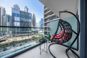 A balcony with a hanging chair, a small table, and a view of a cityscape with modern buildings. - Free housekeeping visits during your stay - StayShort - 1 Bed in Business Bay with Modern Amenities (Business Bay)