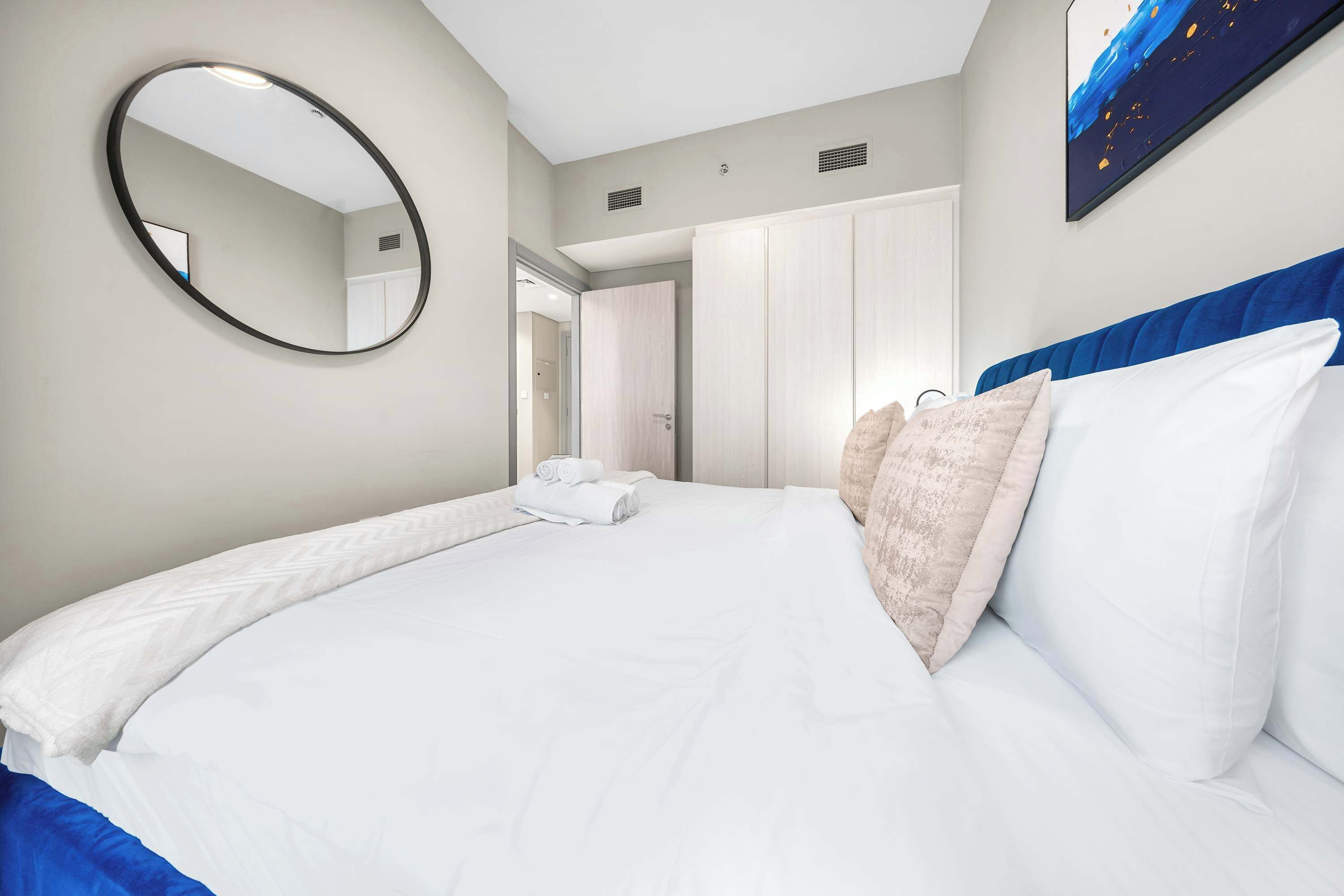 Une chambre d  ’hôtel avec un grand lit, un miroir rond, une armoire et un tableau au mur.