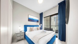 Ein modernes Hotelzimmer mit einem großen Bett, einem Nachttisch mit Lampe, Blick auf die Stadt durch ein großes Fenster und einem Balkon mit blauen Vorhängen.