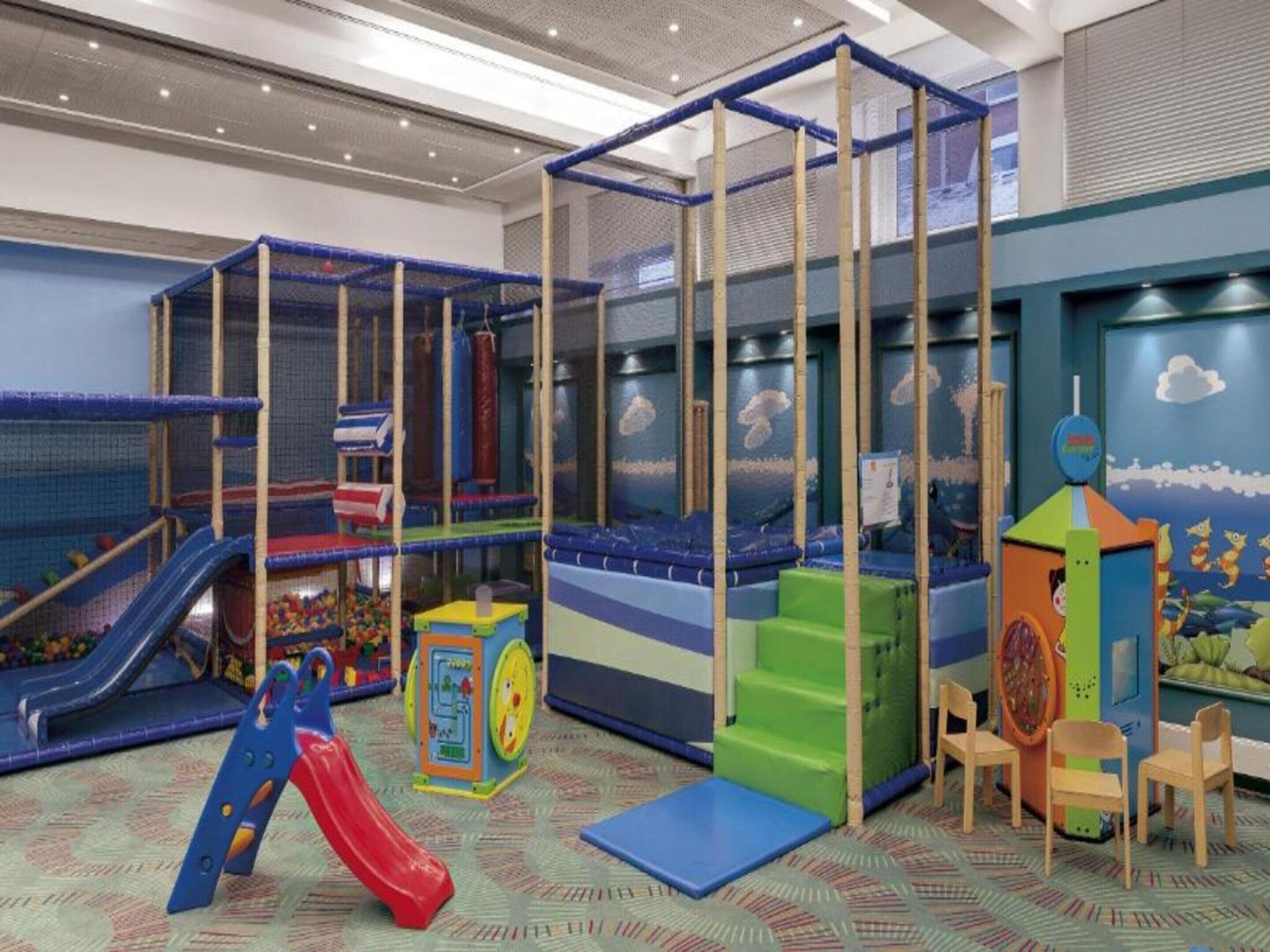 Zona de juegos infantiles con tobogán, estructuras para escalar y piscina de pelotas.