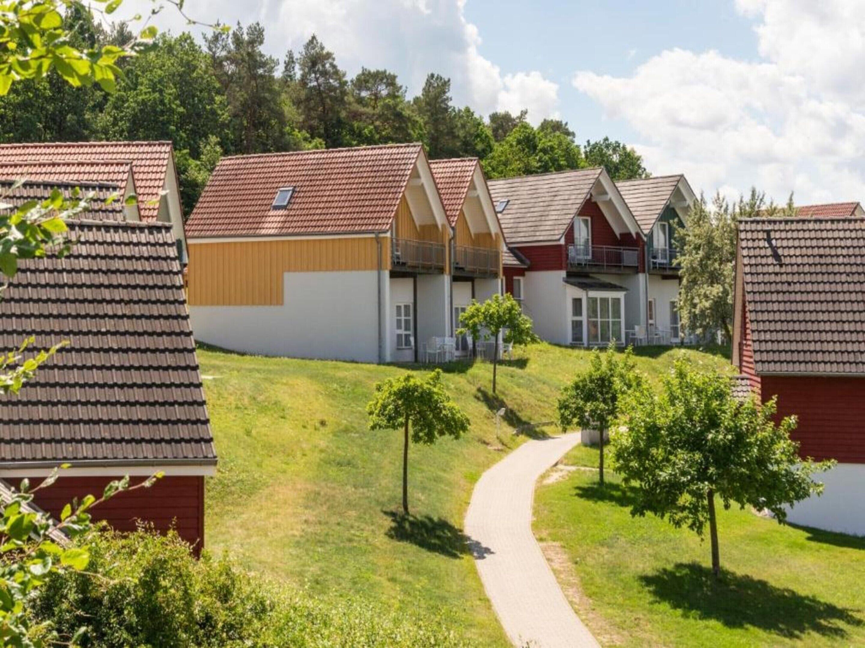 A row of modern houses with sloped roofs, a paved pathway, and a grassy area with trees.